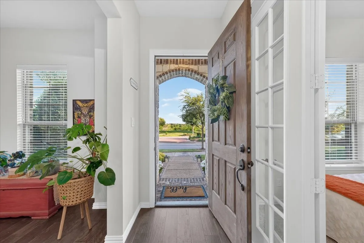 Warm wood-finish flooring extending from the entryway, an arched brick-lined doorway, and a solid wood front door with dark hardware