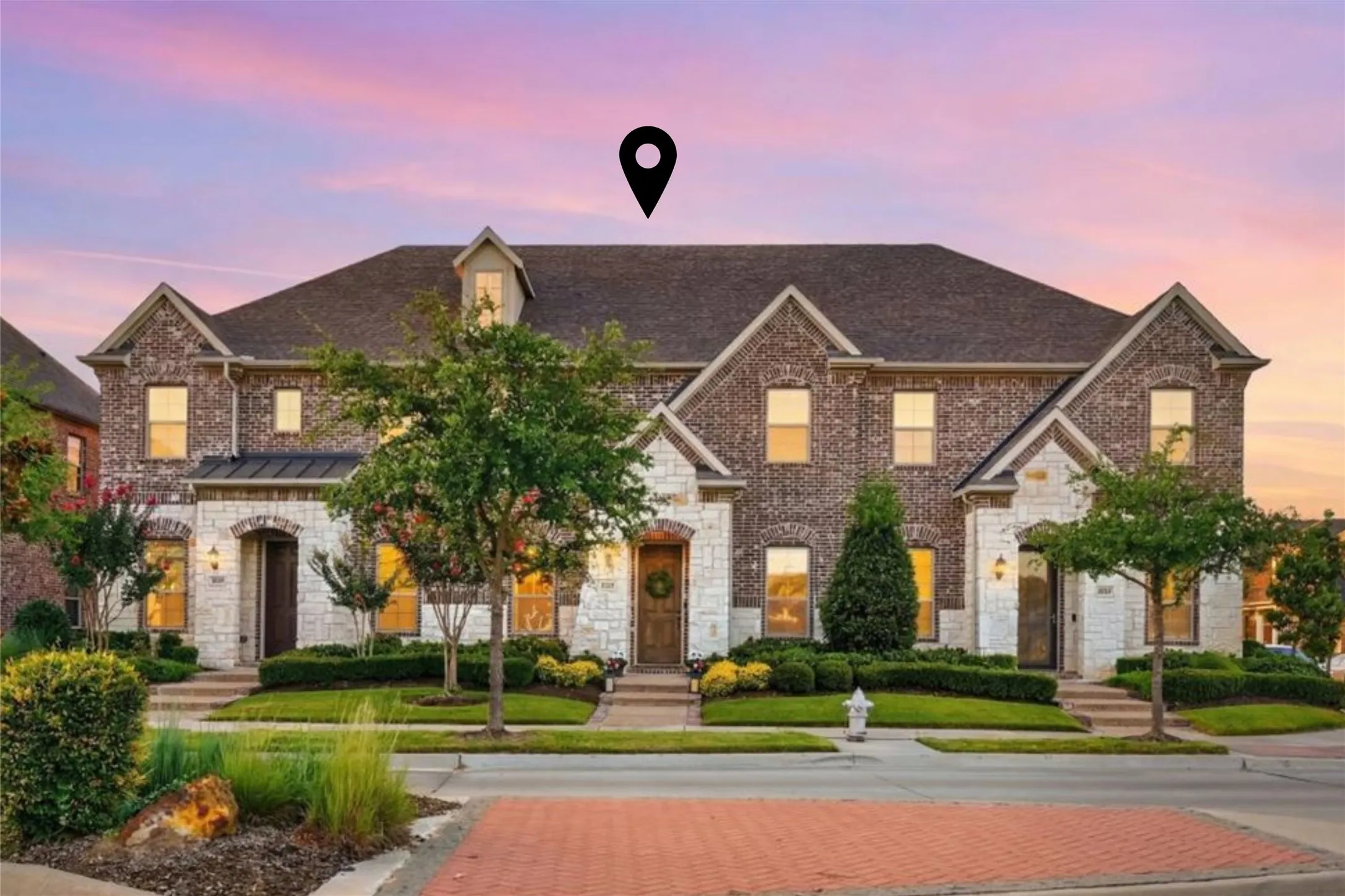 Brick and stone facade townhome featuring gabled rooflines, dormer windows, a covered entry, and mature landscaping
