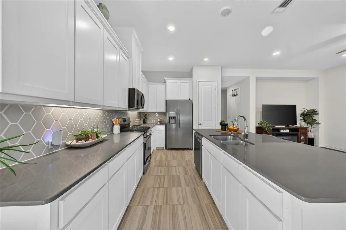 Modern kitchen featuring white shaker cabinetry, dark countertops, a hexagonal tile backsplash, and stainless steel appliances