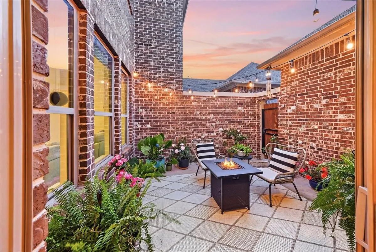 Private courtyard patio featuring brick walls, string lighting, and a square paver surface
