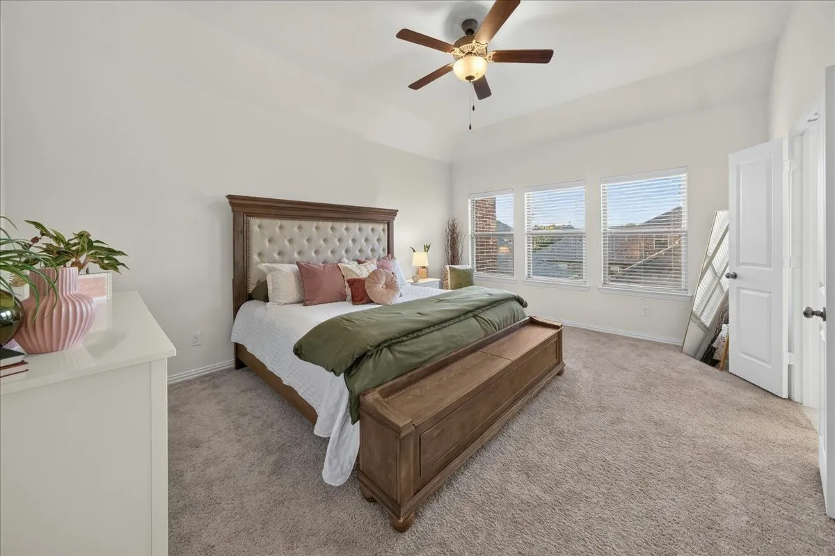 Spacious room featuring vaulted ceilings, plush carpet flooring, and abundant natural light from a wall of three windows