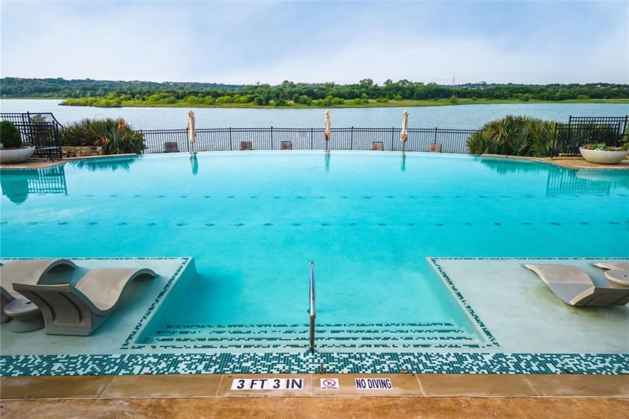 Infinity-edge pool featuring a tiled perimeter, integrated lounge seating, and steps for pool entry