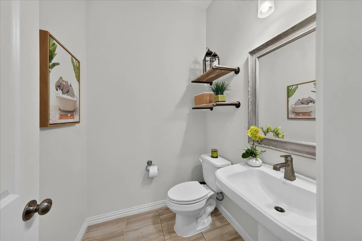 Pedestal sink with a bronze-finish faucet, framed mirror, and wood-finish open shelving
