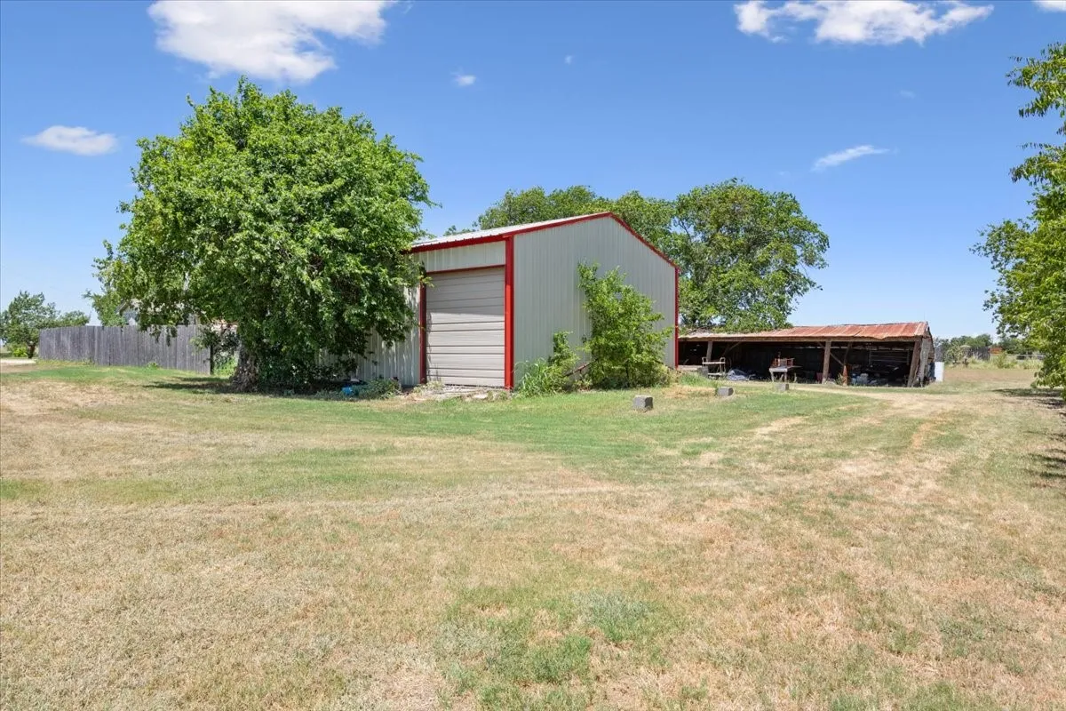 Metal outbuilding with a roll-up door and red trim, accompanied by a separate open-air structure