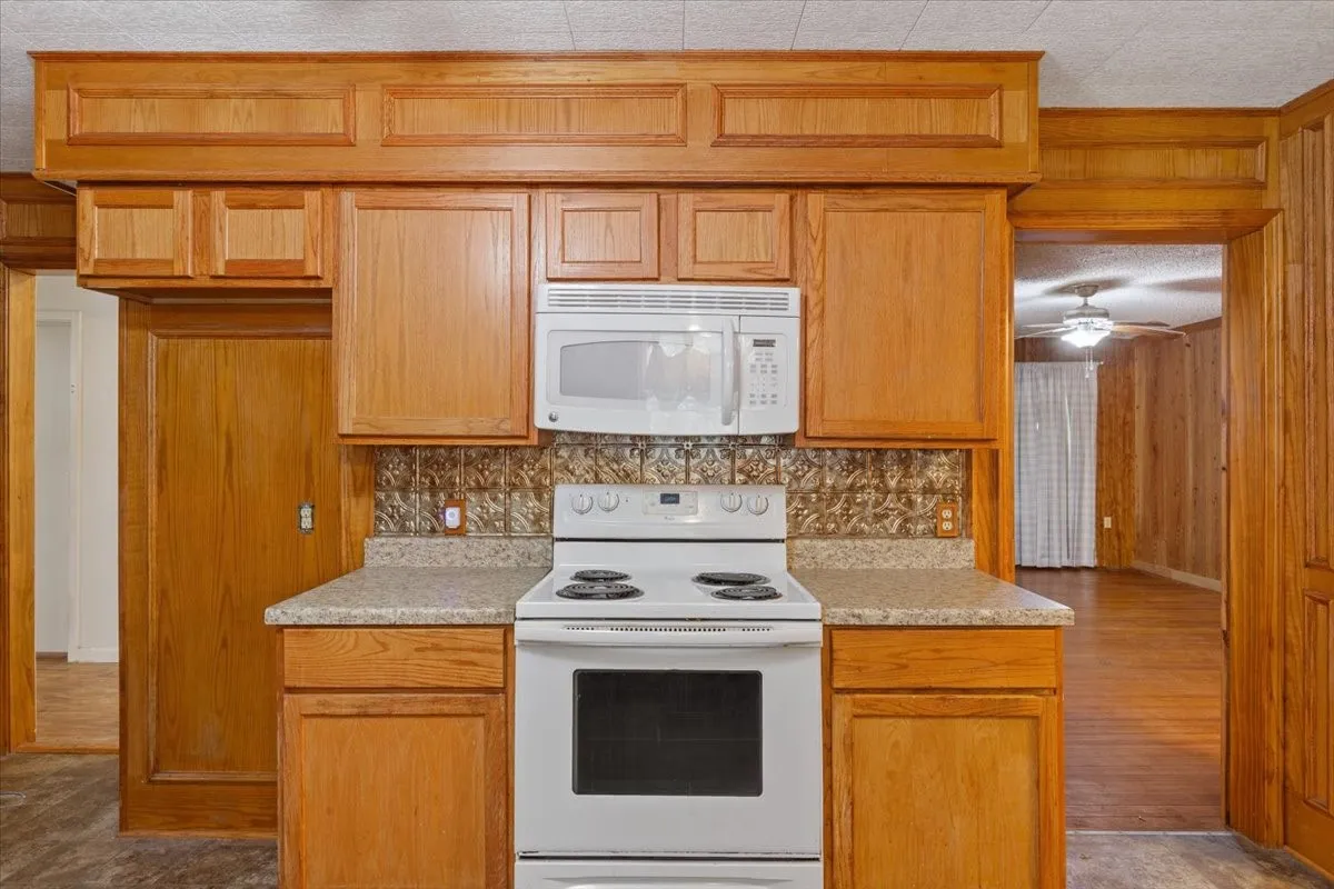 Kitchen featuring wood-finish cabinetry, built-in microwave, white electric range, and patterned backsplash