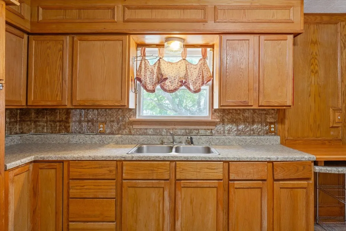 Kitchen area featuring wood cabinetry, textured backsplash, and a double basin stainless steel sink