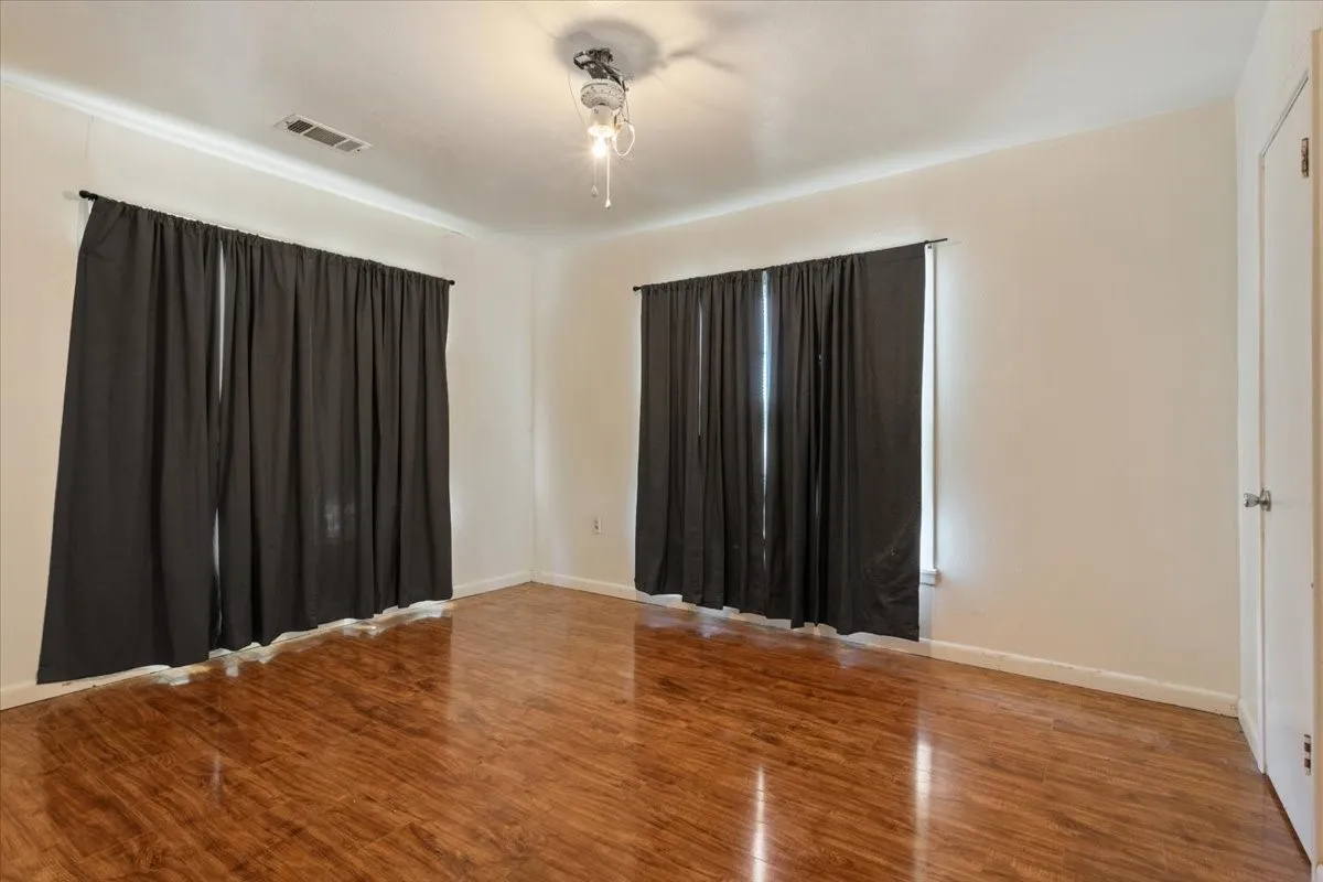 Expansive room featuring wood-finish flooring, two window openings, crown molding, and a ceiling-mounted light fixture