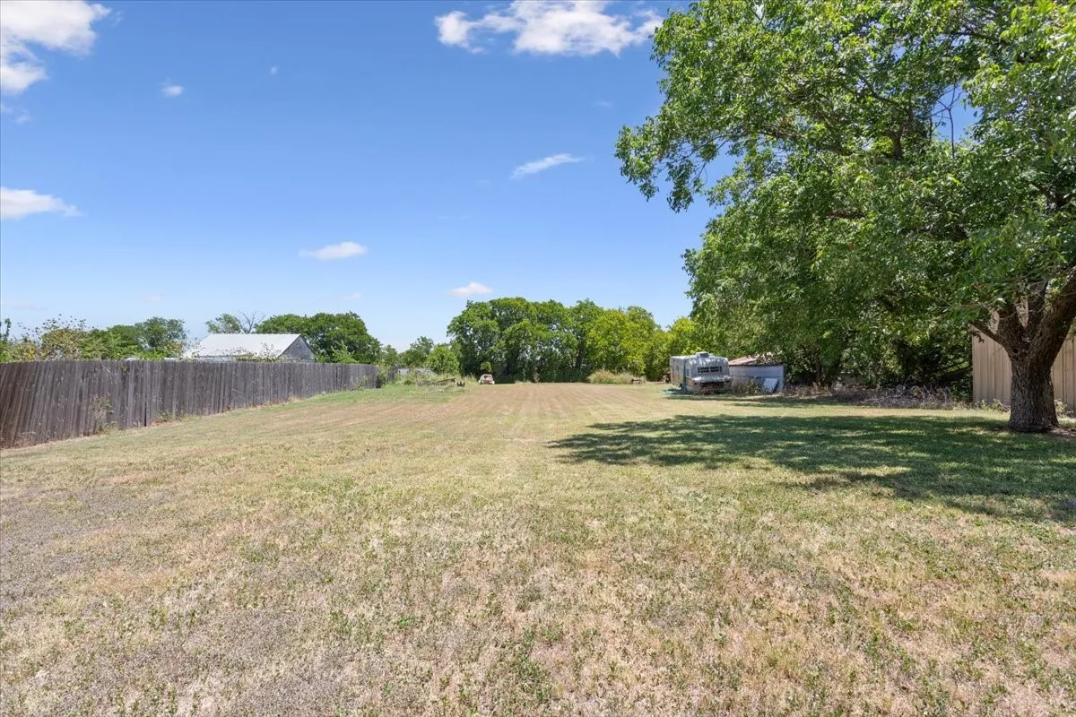 Expansive open lot featuring a large mature tree, wood privacy fencing, and distant green foliage
