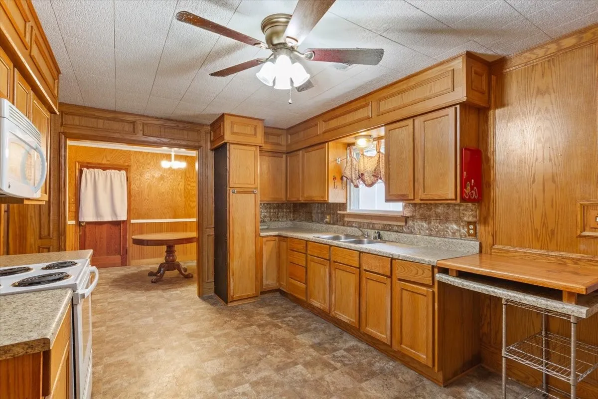 Kitchen featuring extensive wood cabinetry, L-shaped countertop, double basin sink, and ceiling fan
