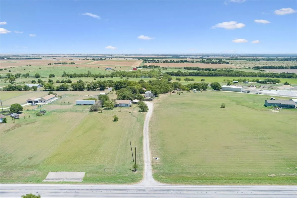 Extensive rural property featuring a long gravel driveway, multiple structures, and expansive green fields extending to the horizon