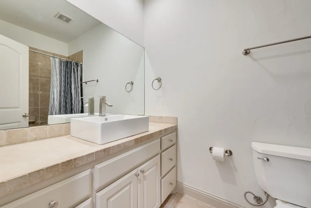 Bathroom featuring a vessel sink with a brushed nickel faucet, light-toned countertop, white cabinetry with silver-toned hardware, and a full-width mirror