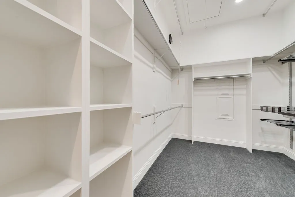 Spacious walk-in closet featuring built-in shelving, hanging rods, and dark gray carpeting