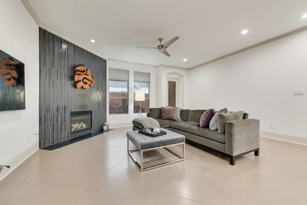 Living space featuring a tiled fireplace with a dark surround, light-toned tile flooring, recessed lighting, a ceiling fan, and large windows with privacy shades