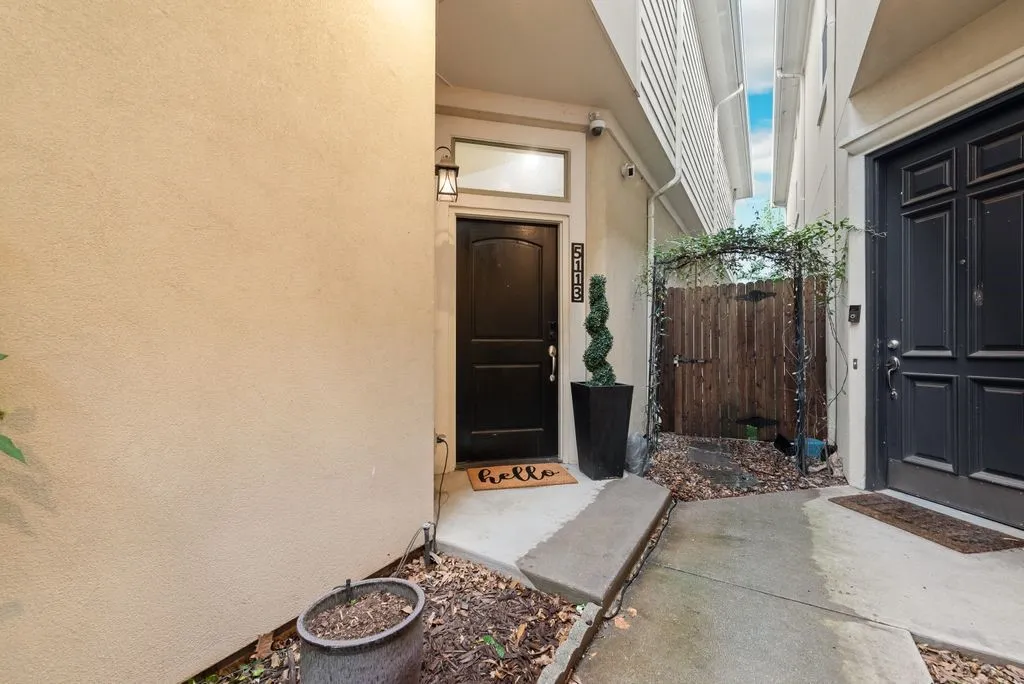 Stucco exterior with a dark paneled entry door, transom window, and exterior wall lantern