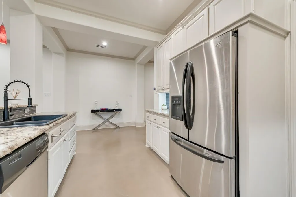 Modern kitchen featuring a stainless steel refrigerator, white cabinetry, granite countertops, and a double basin sink with a matte black faucet