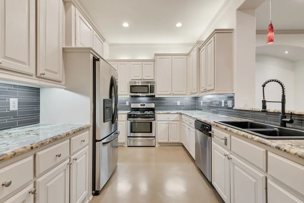 Kitchen featuring light-toned cabinetry, stainless steel appliances, granite countertops, and a subway tile backsplash