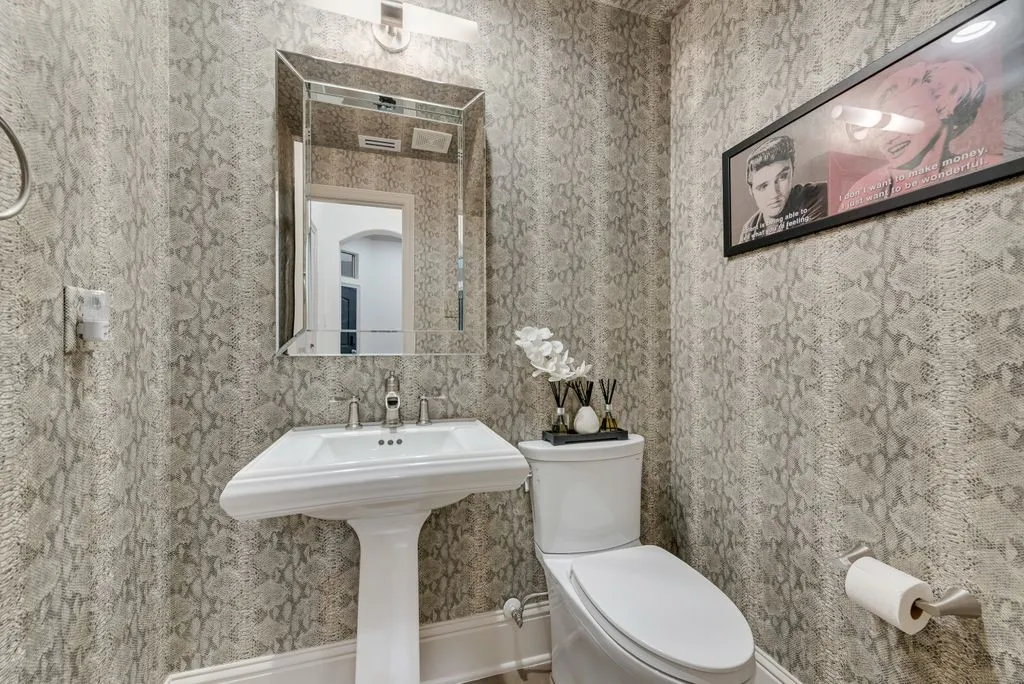 Pedestal sink with polished chrome faucet set, complemented by a beveled mirror and wall-mounted lighting