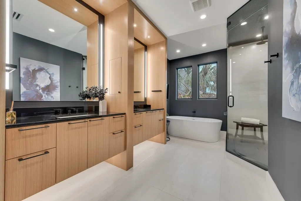 Contemporary bathroom featuring a freestanding soaking tub, dual vanity with black countertops, and a glass-enclosed shower