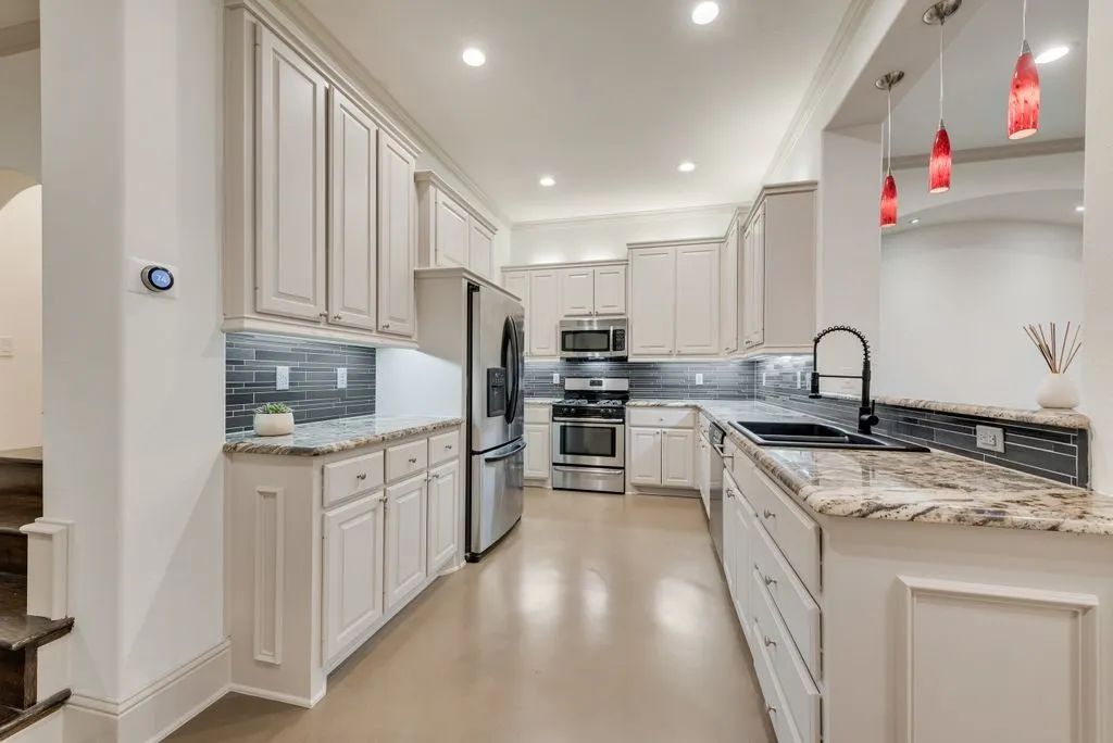 Modern kitchen featuring extensive white cabinetry, stainless steel appliances, a dark tile backsplash, and light-toned countertops