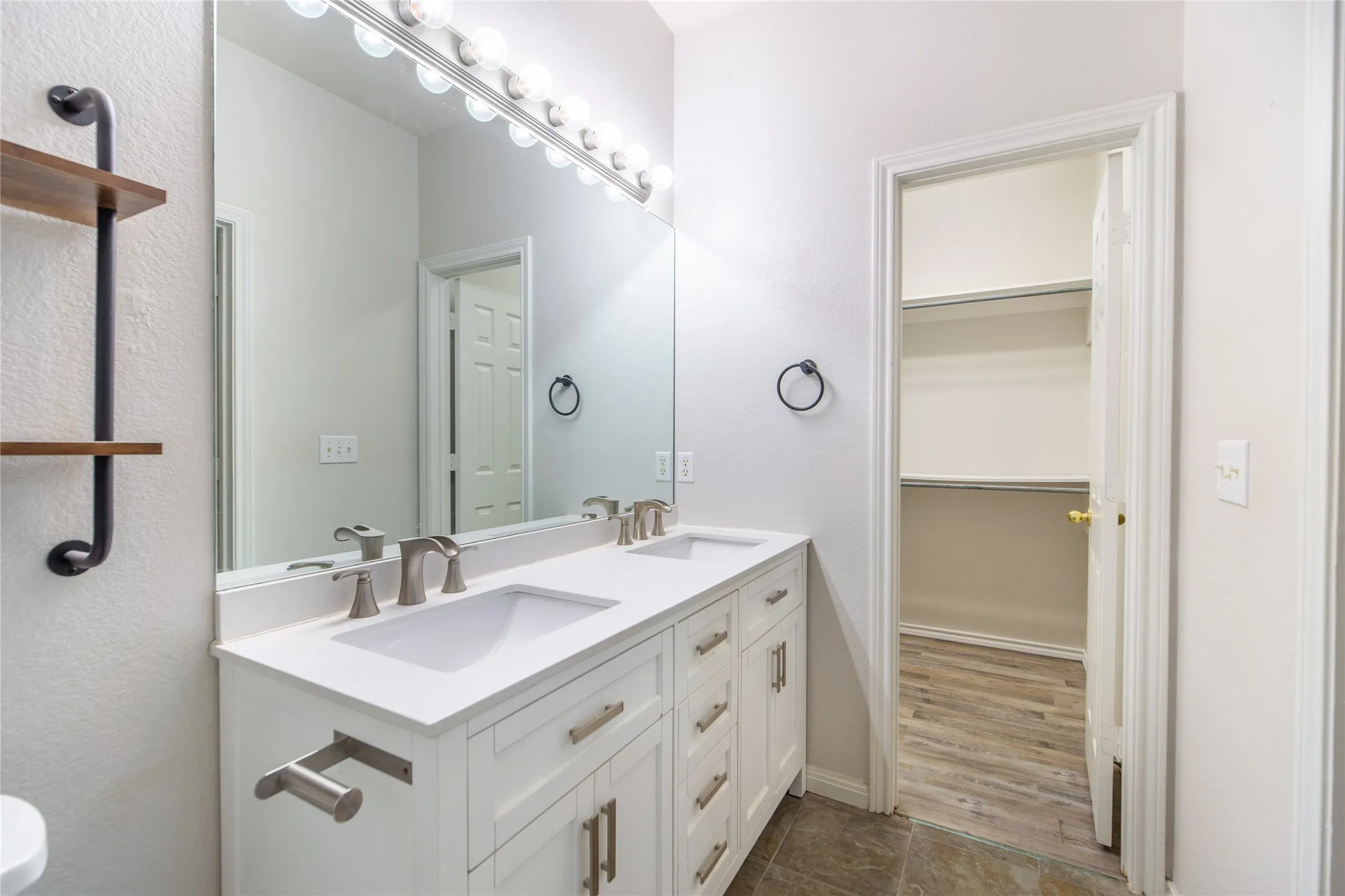 Bathroom featuring a double vanity with white cabinetry and integrated sinks, brushed nickel fixtures, and a large wall-mounted mirror with overhead lighting