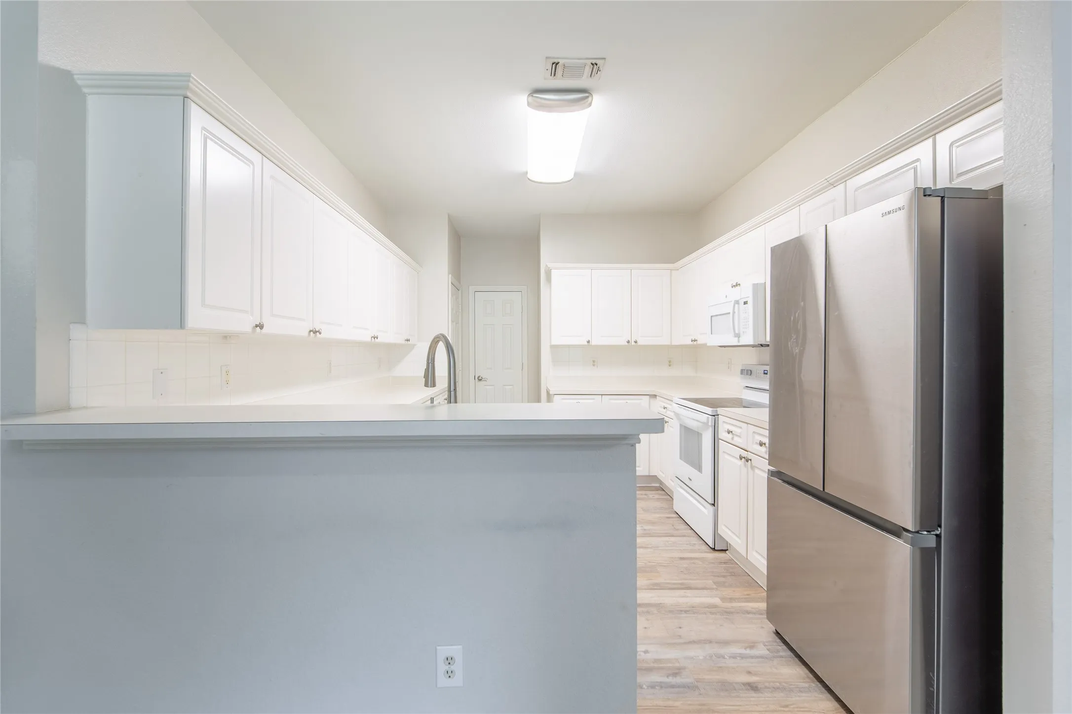 Bright kitchen featuring white cabinetry, light countertops, wood-finish flooring, a stainless steel refrigerator, and a stainless steel gooseneck faucet