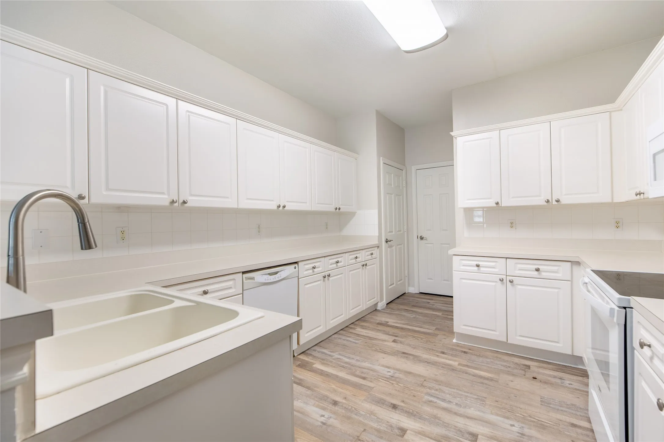 Kitchen featuring extensive white cabinetry, wood-finish flooring, a double basin sink with a high-arch faucet, white appliances, and light countertops