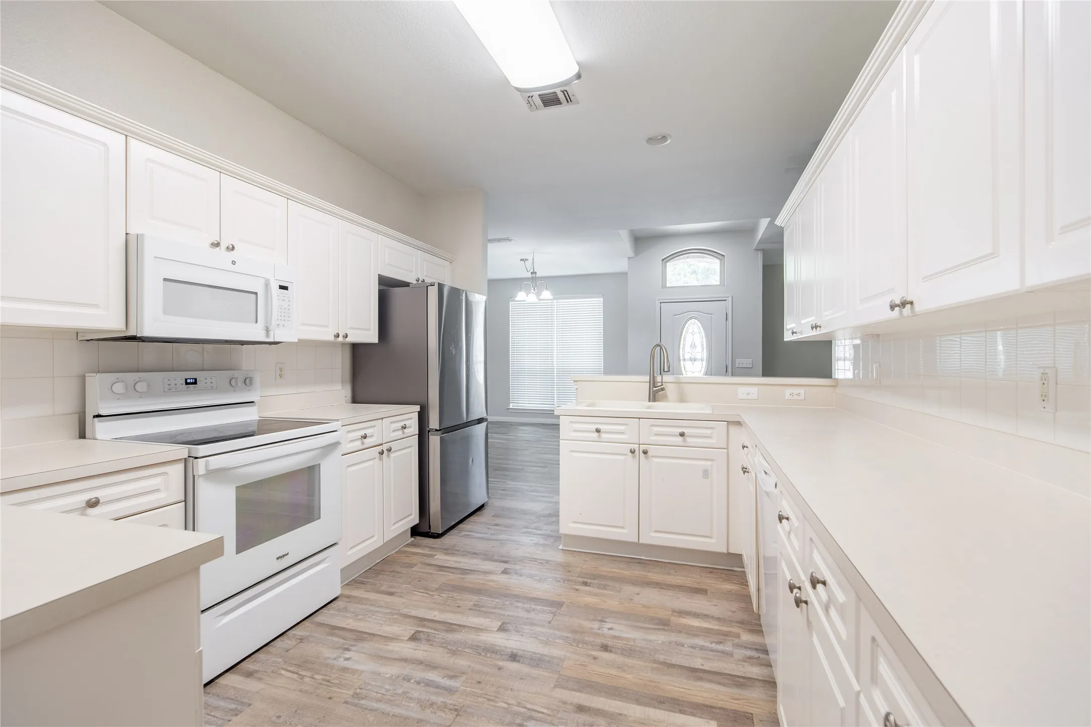 Kitchen featuring white cabinetry, light countertops, wood-finish flooring, and stainless steel appliances