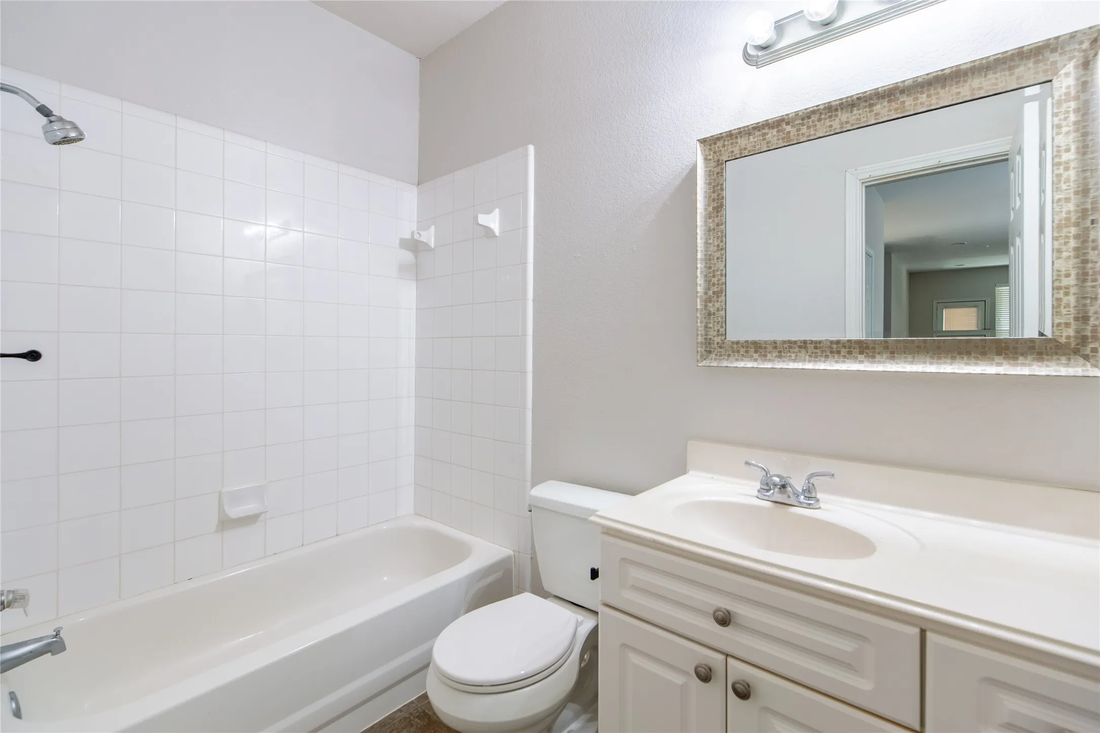 Bathroom featuring a white subway tile shower surround, a built-in bathtub, and a single-sink vanity with a mosaic-framed mirror