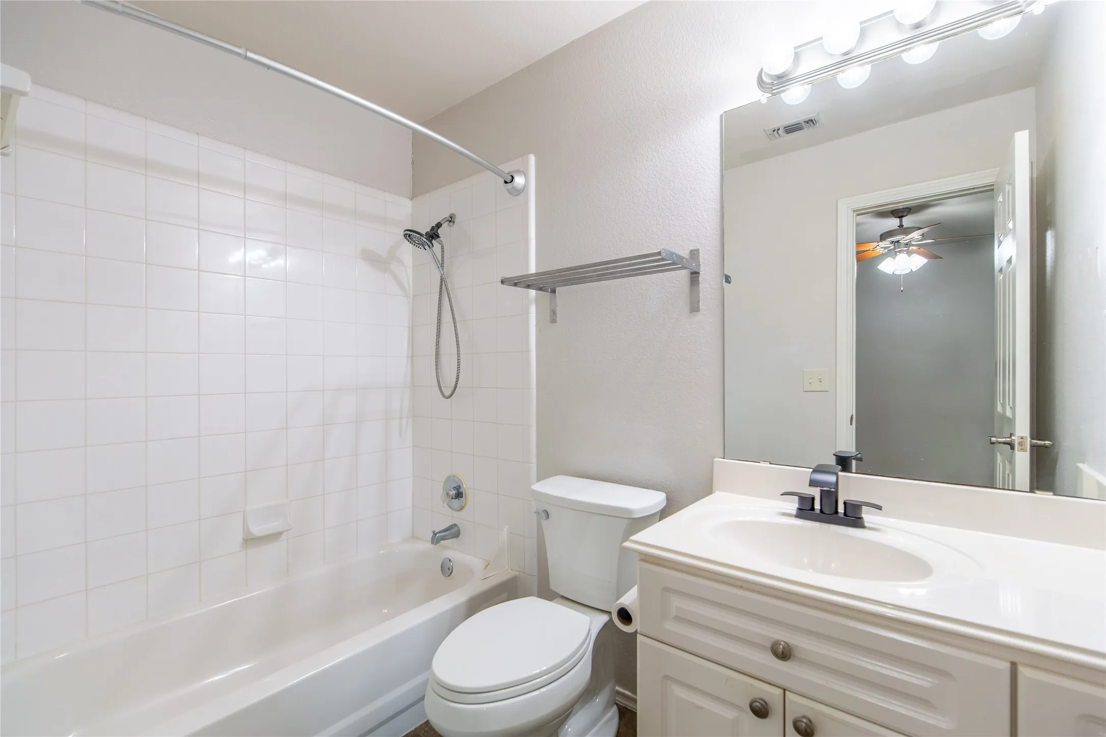 Bathroom featuring a white vanity with an integrated sink, black hardware, a wall-mounted mirror, and overhead strip lighting