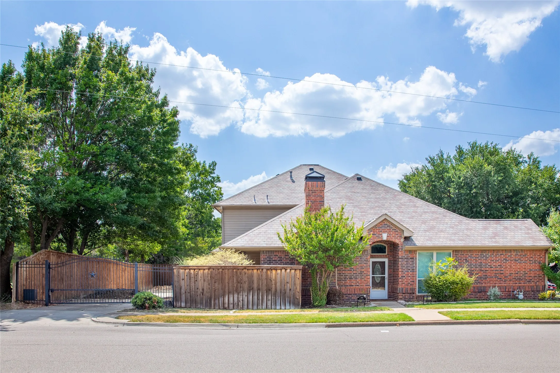 Brick exterior featuring an arched entryway, mature landscaping, and a side-facing garage with a wrought iron and wood privacy gate