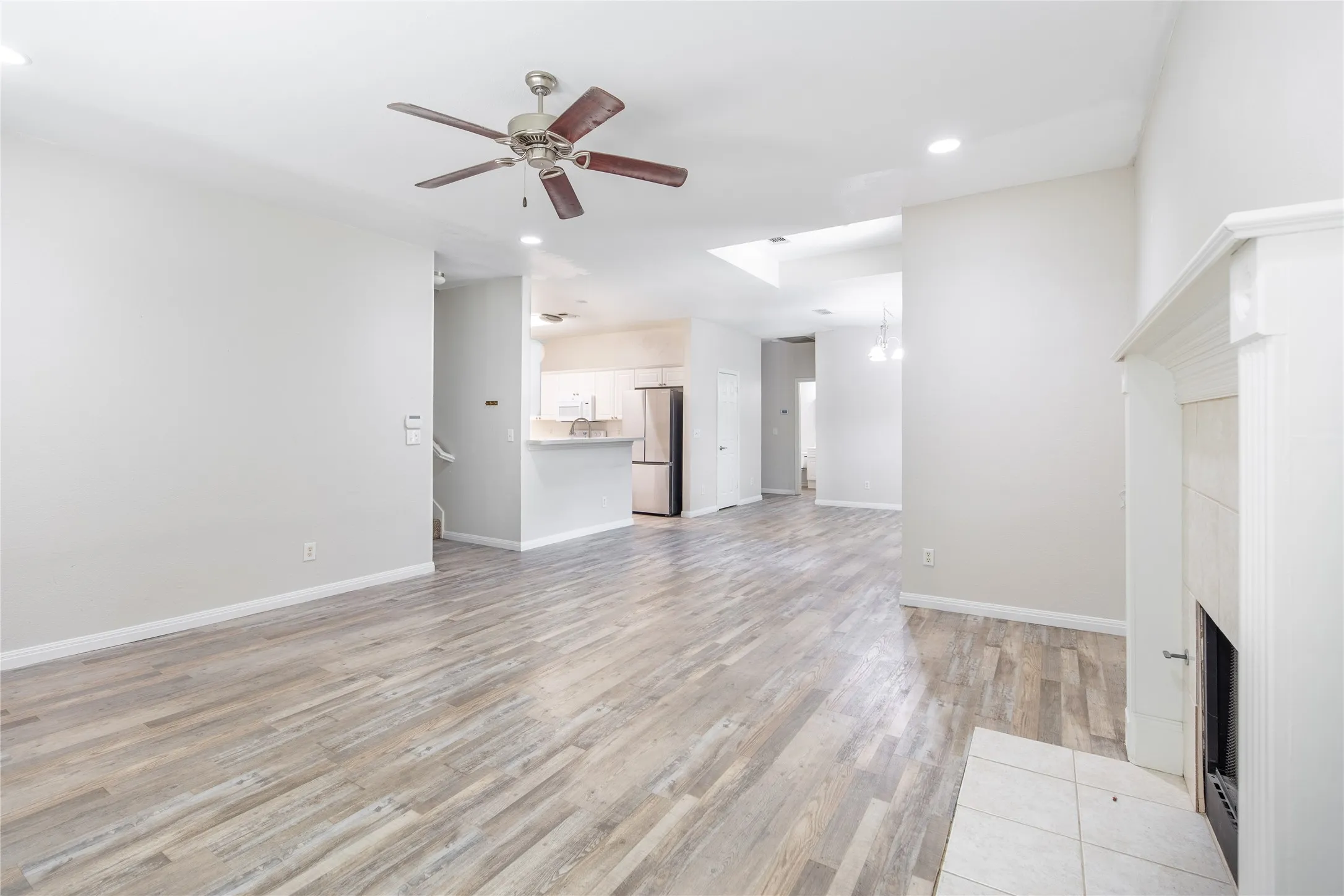 Spacious living area featuring wood-finish flooring, a traditional fireplace with a white mantel, and a ceiling fan