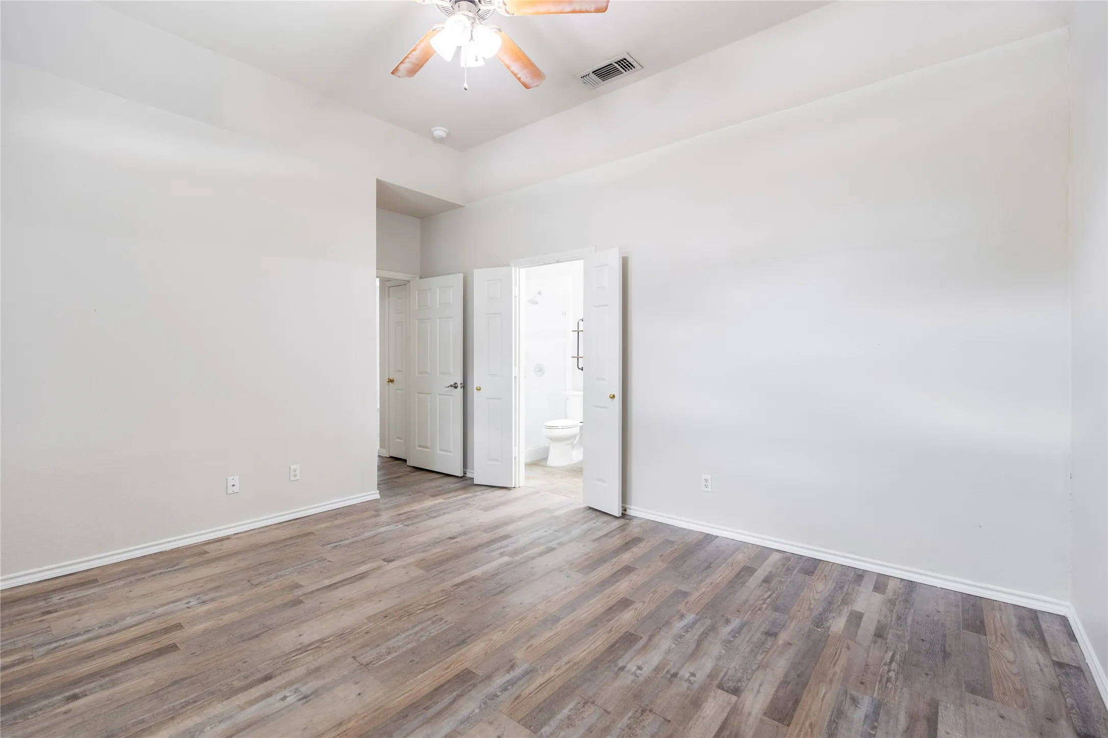 Spacious interior room featuring wood-finish flooring, white baseboards, and neutral wall tones