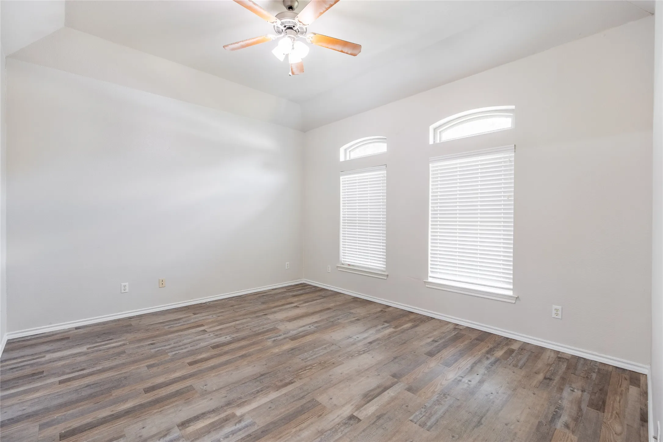 Spacious room featuring wood-finish flooring, light-toned walls, and a ceiling fan