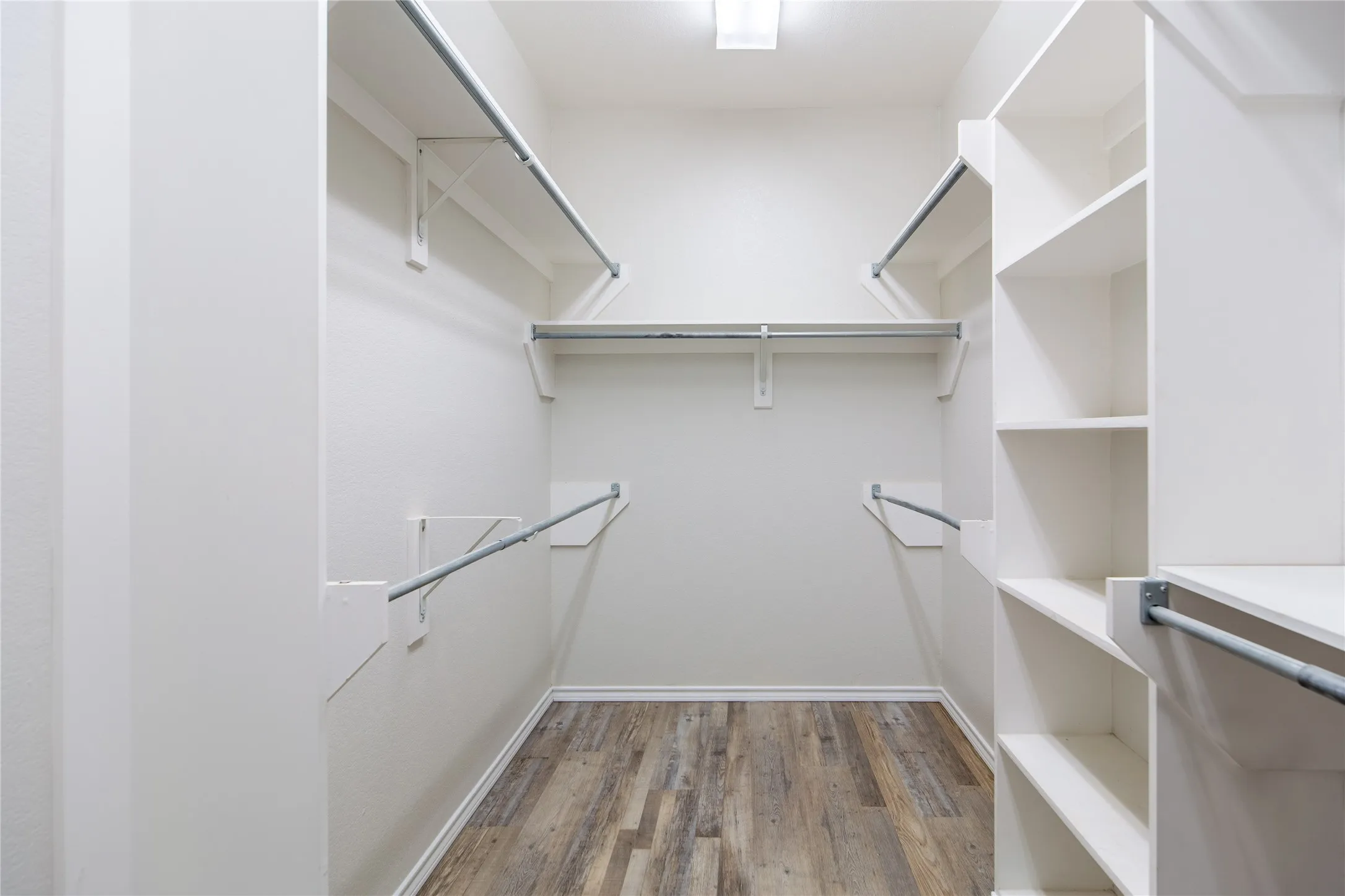 Walk-in closet featuring wood-finish flooring, white shelving, multiple hanging rods, and recessed lighting