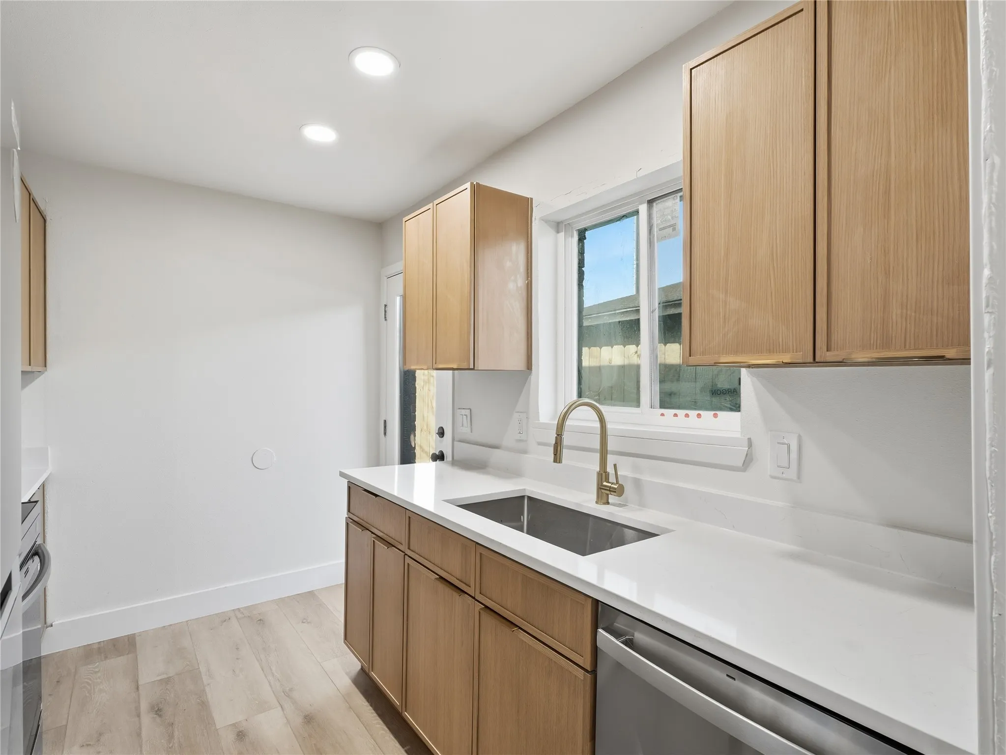 Kitchen featuring light wood-finish cabinetry, white countertops, stainless steel sink with gold-tone faucet, and recessed lighting
