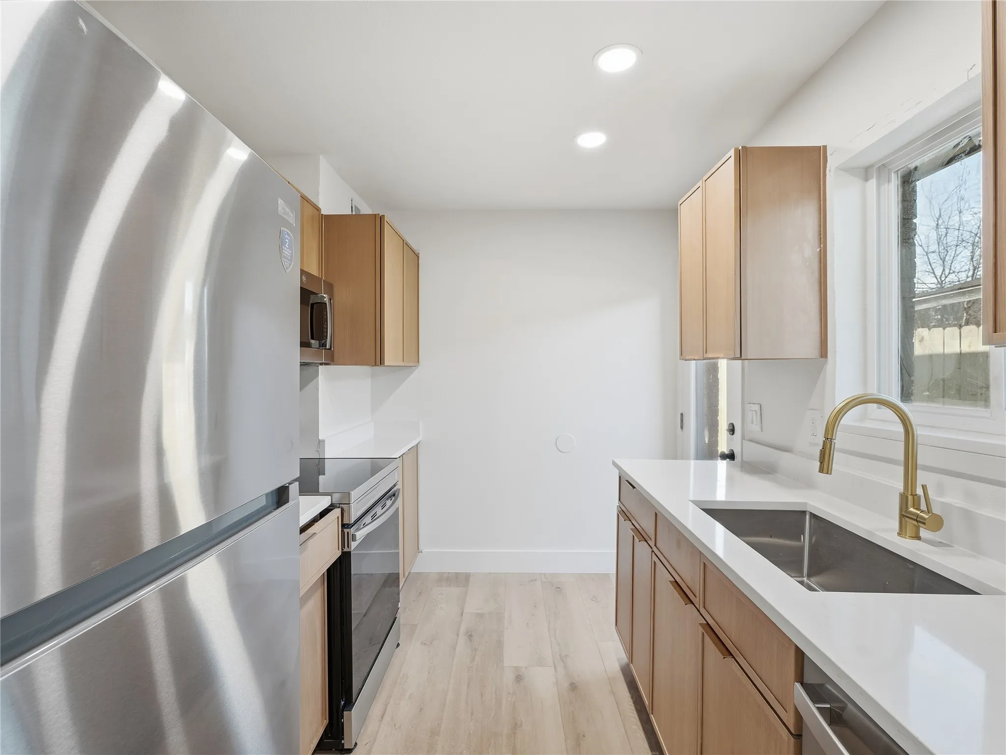 Kitchen featuring wood-finish cabinetry, stainless steel appliances, white countertops, a single basin sink with a gold-tone faucet, and recessed lighting