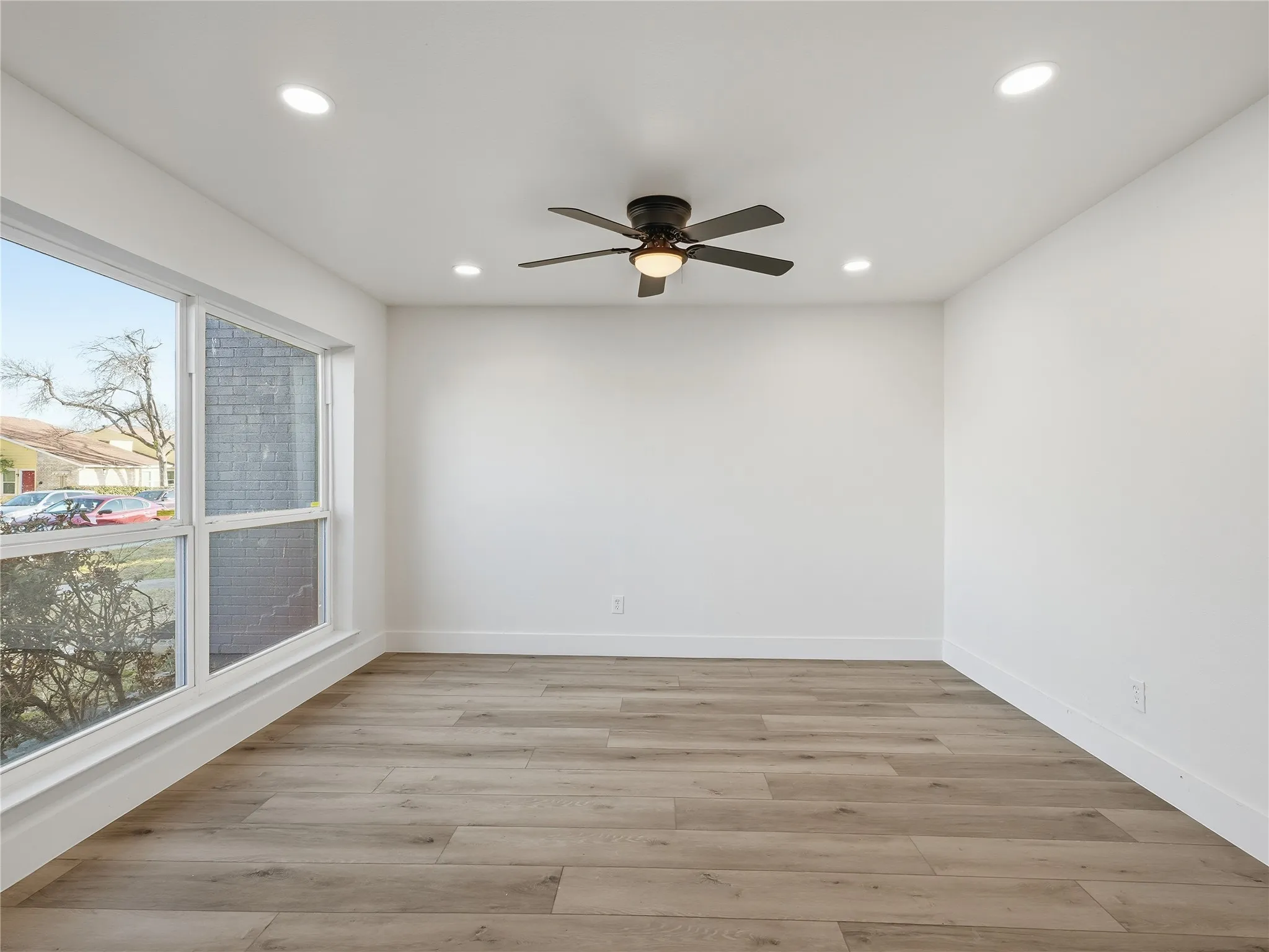 Spacious room featuring wood-finish flooring, white baseboards, and bright white walls