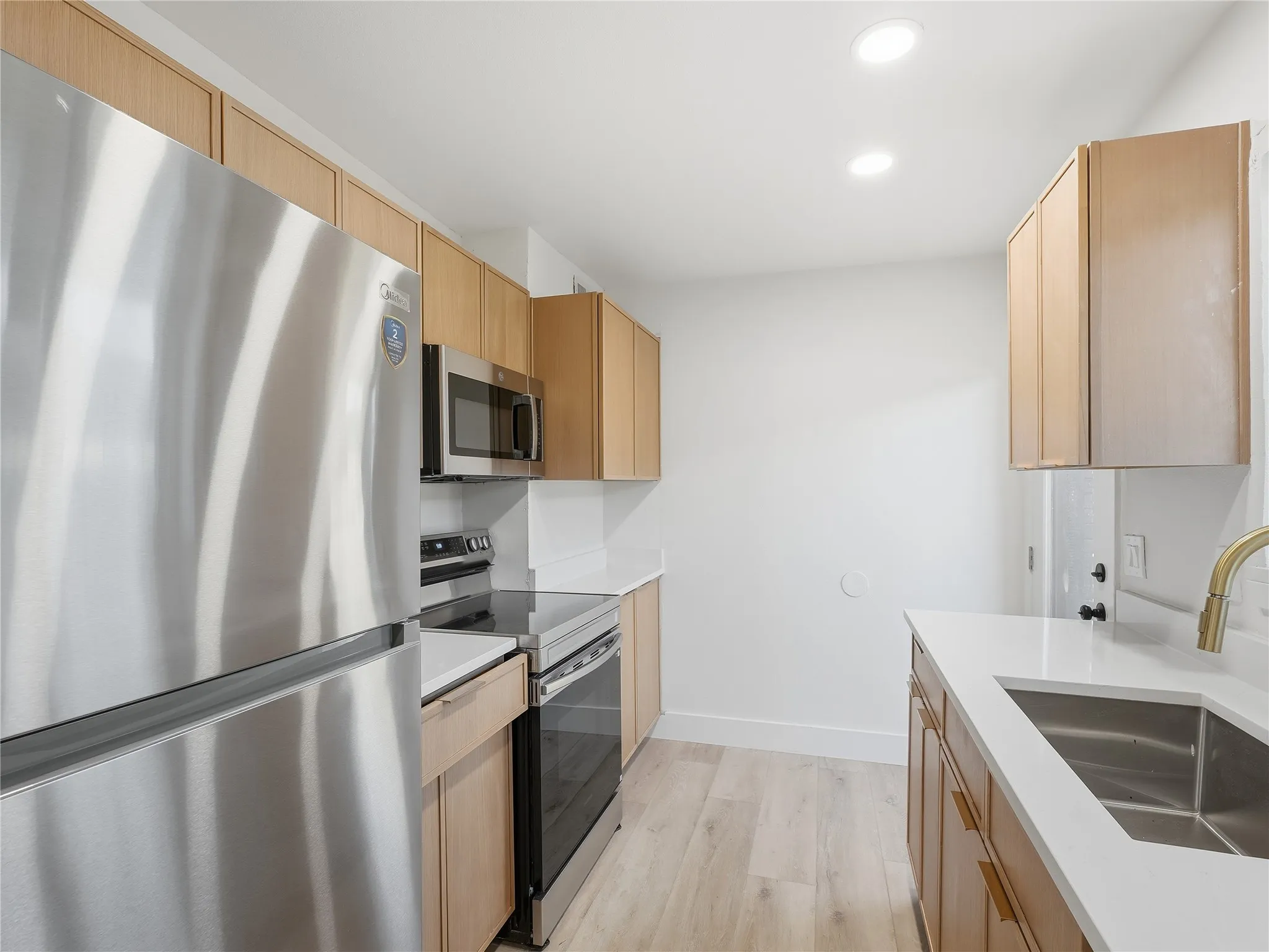 Kitchen featuring a stainless steel refrigerator, stainless steel electric range, stainless steel over-the-range microwave, light wood-finish cabinetry, and light countertops