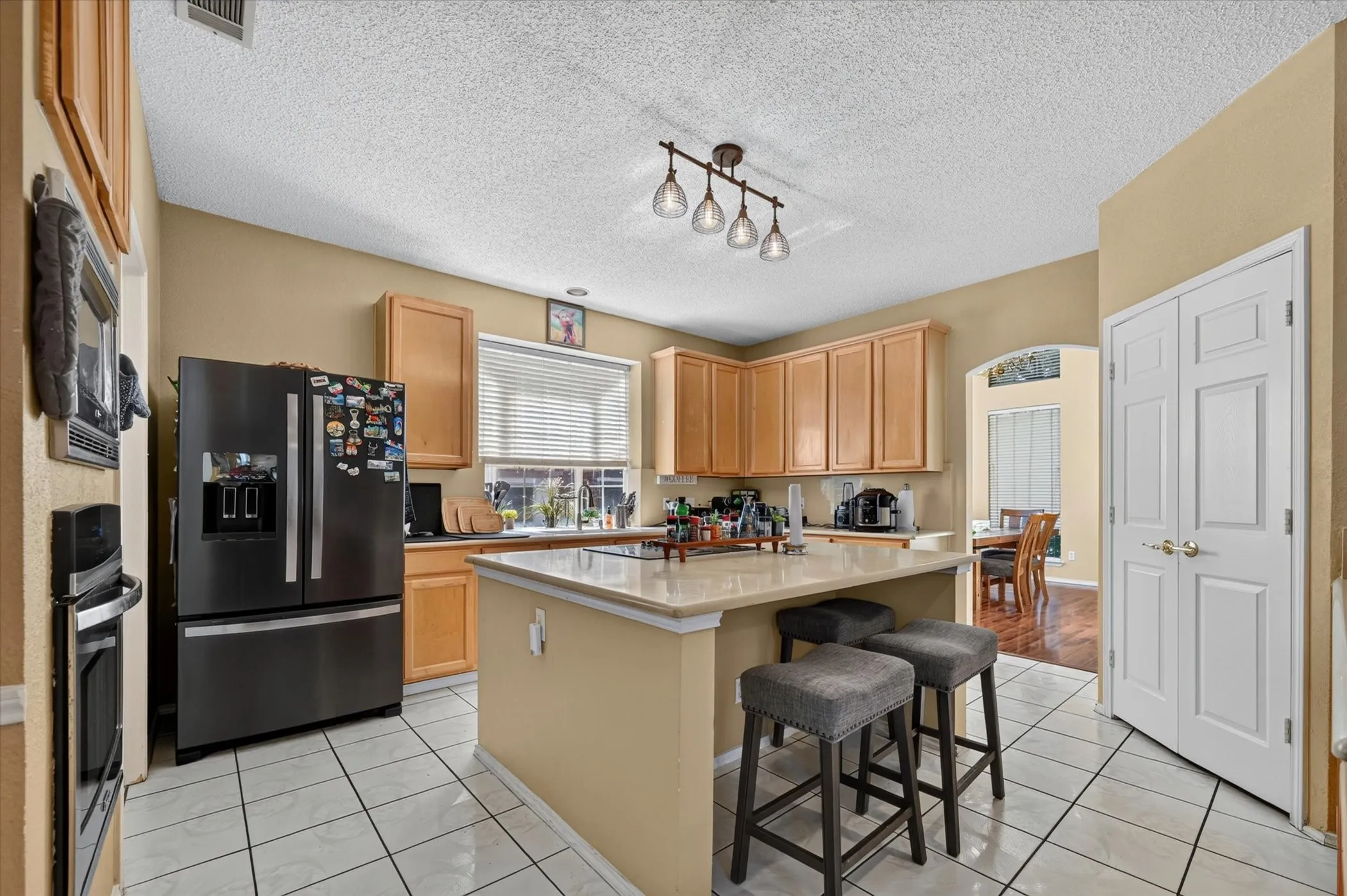 Kitchen featuring an island with countertop seating, light wood-finish cabinetry, a built-in oven, and a double-door pantry