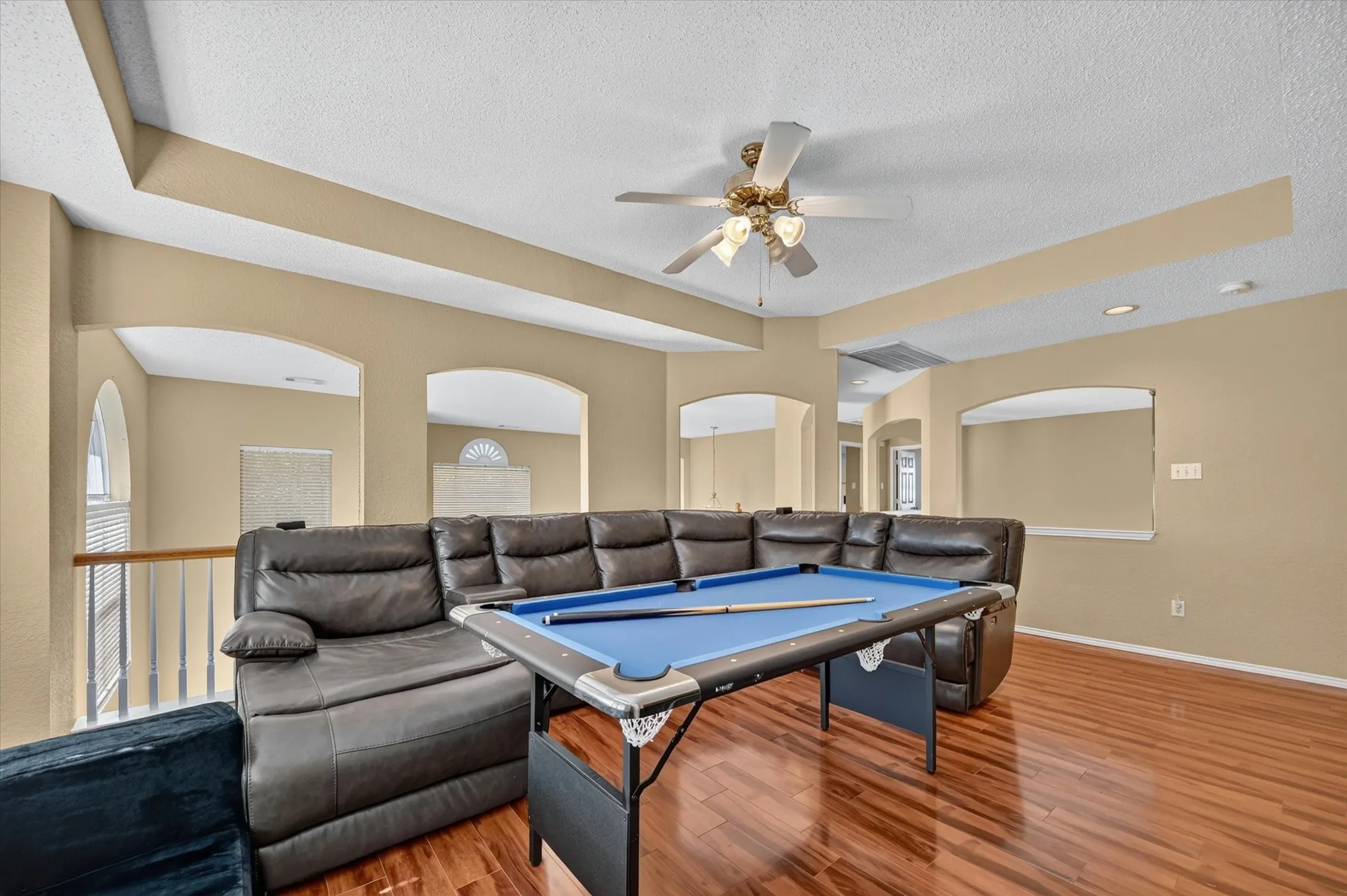 Upper-level room featuring wood-finish flooring, a ceiling fan, and arched wall openings overlooking a lower level