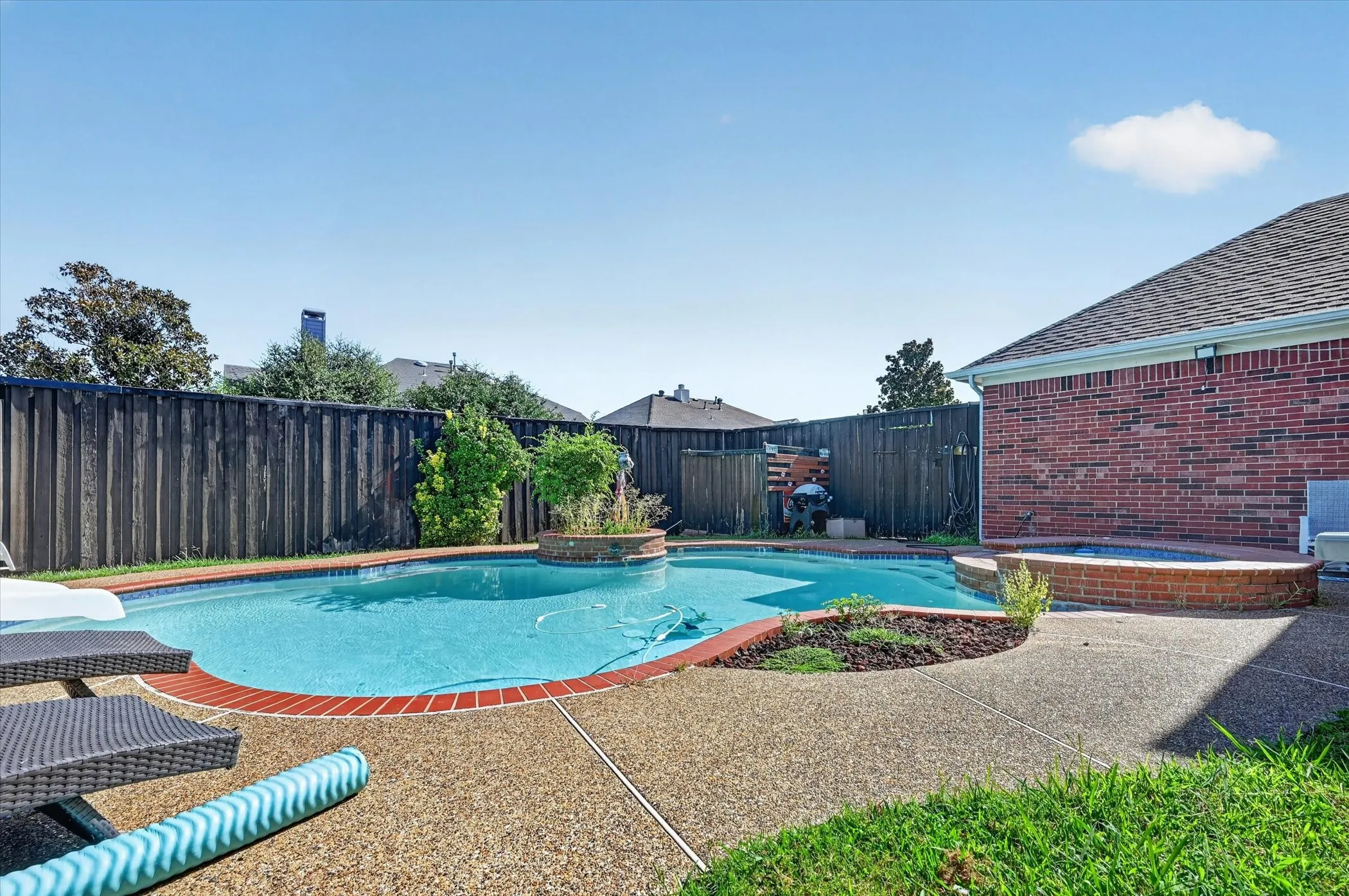 Backyard entertainment space featuring a swimming pool, integrated spa, and exposed aggregate patio