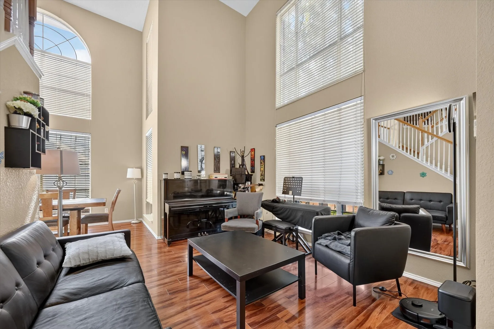 Vaulted ceilings with multiple windows, including an arched transom window, define this open living area featuring wood-finish flooring and neutral-toned walls