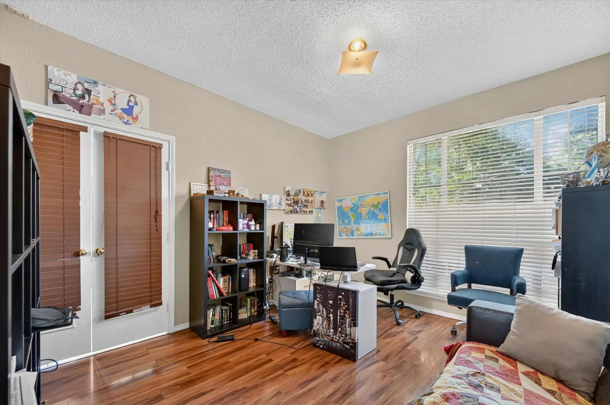 Spacious room featuring wood-finish flooring, ample natural light from a large window, and double doors with privacy blinds