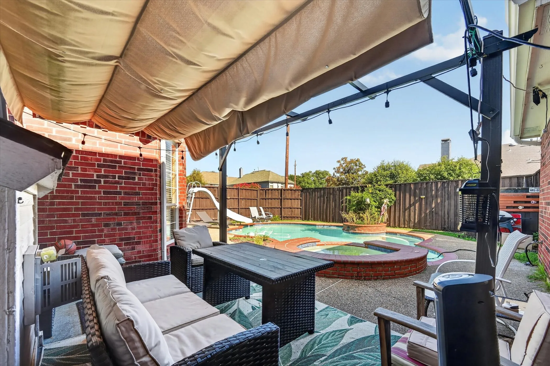 Covered patio featuring a brick exterior wall, string lighting, and a retractable canopy