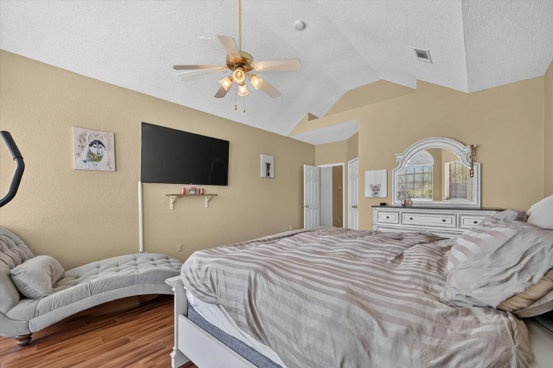 Room featuring vaulted ceilings, wood-finish flooring, a ceiling fan with integrated lighting, and a neutral wall color