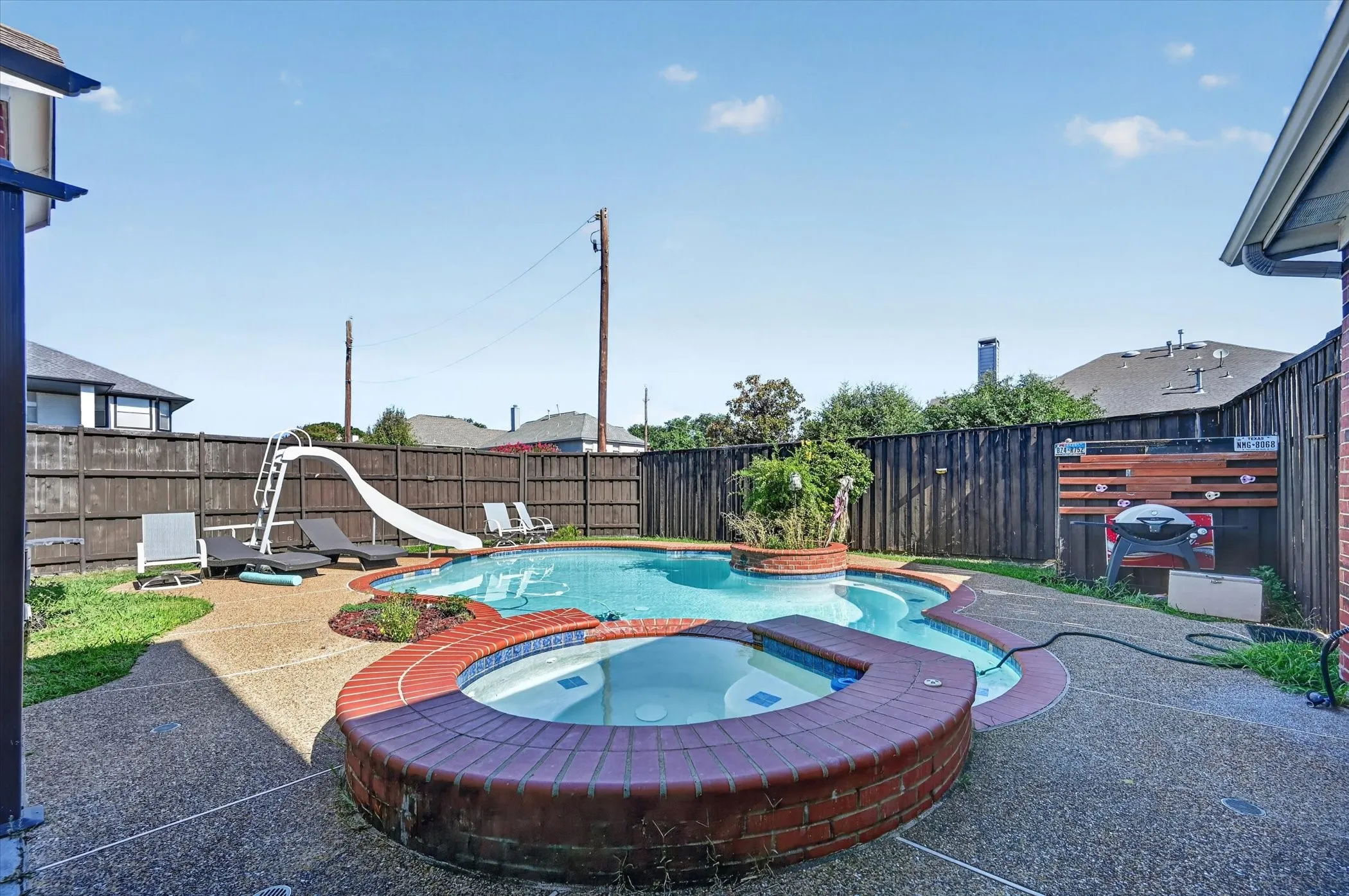 Outdoor living space featuring a freeform swimming pool and an integrated hot tub with brick surround