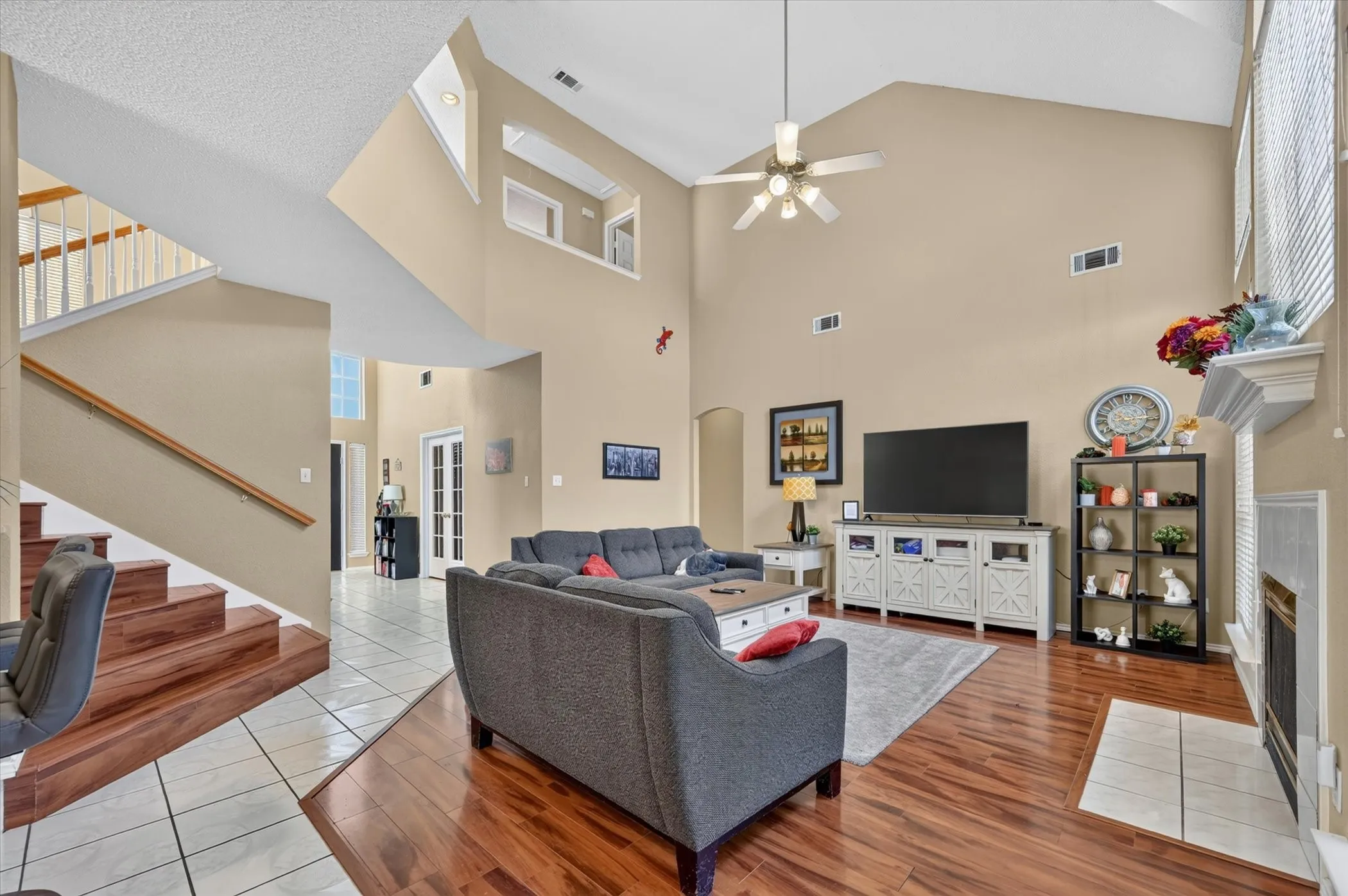 Two-story living area featuring vaulted ceilings, wood-finish flooring, a fireplace with a tile hearth, and a staircase with a wood handrail