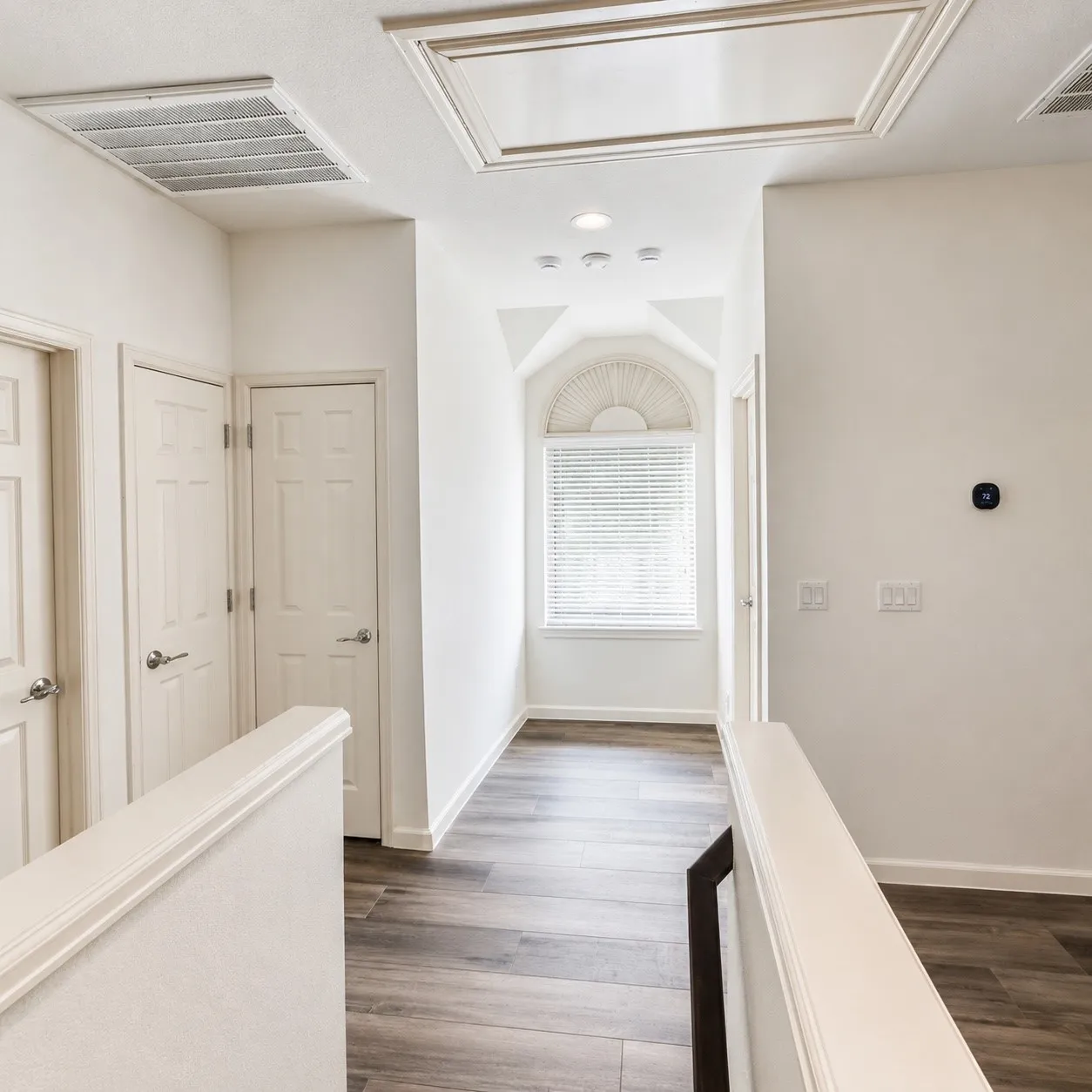 Hallway featuring wood-finish flooring, white doors, and a vaulted ceiling with an arched window
