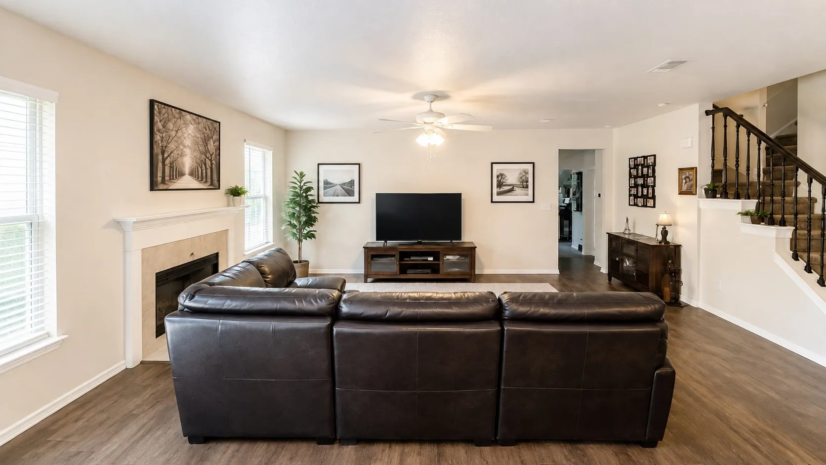 Open-concept living space with wood-finish flooring, a ceiling fan, and a fireplace featuring a light-colored mantel