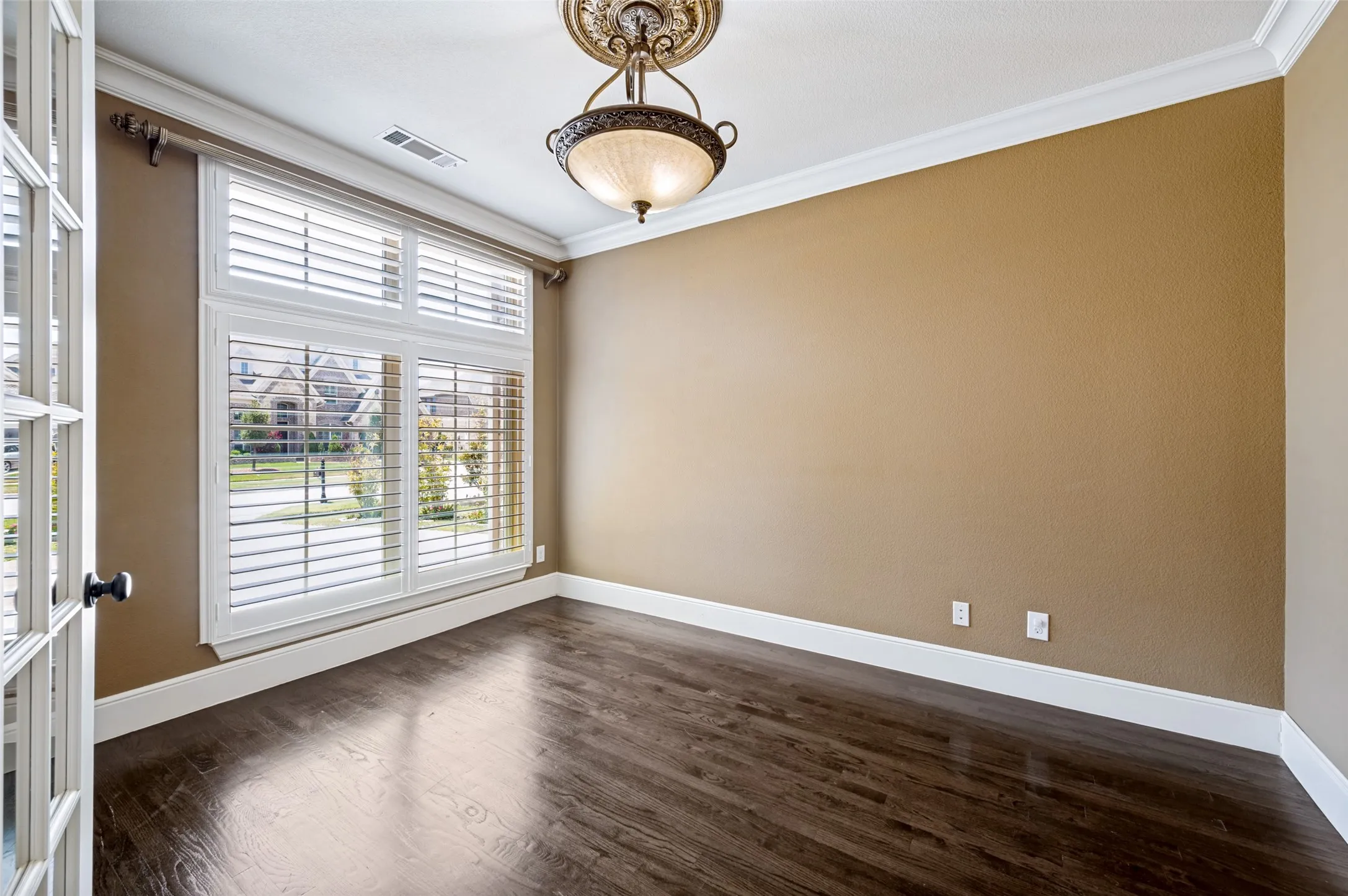 Elegant home office or formal dining space showcasing warm, neutral walls with crisp white trim, rich wood-finish flooring, and abundant natural light from expansive multi-pane French doors and transom windows
